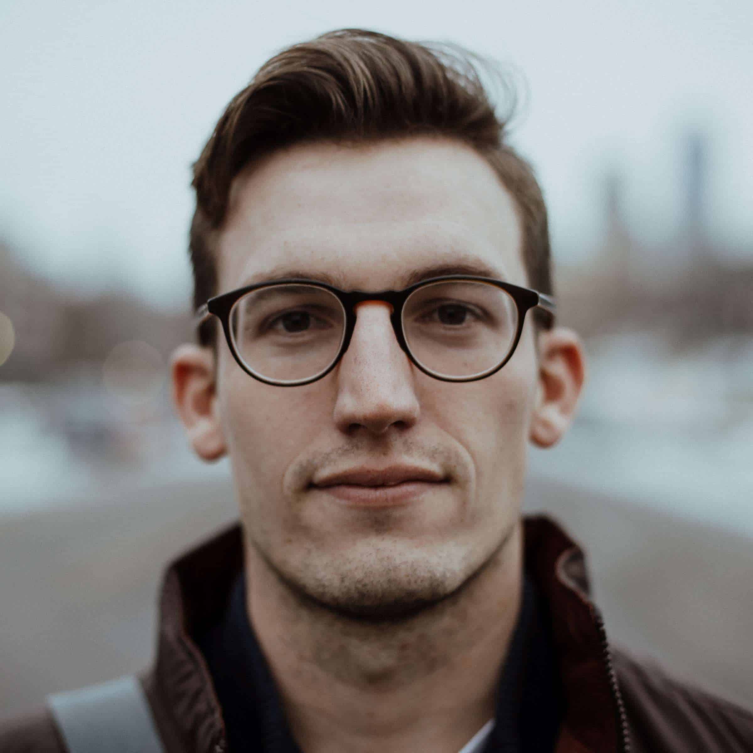 Man with short hair and round glasses looking at the camera
