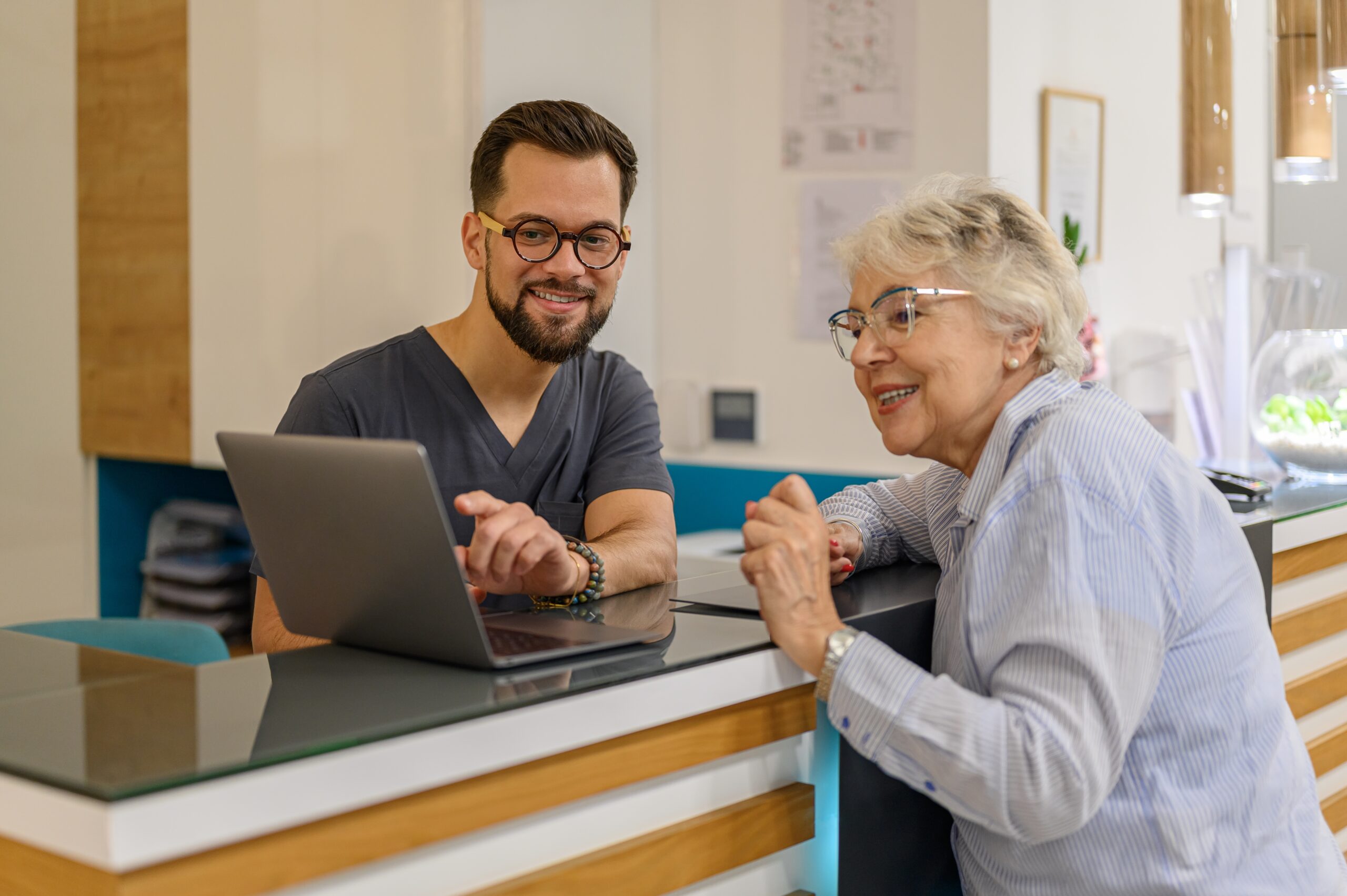 Male Doctor Showing Laptop To Smiling Senior Woman at Reception