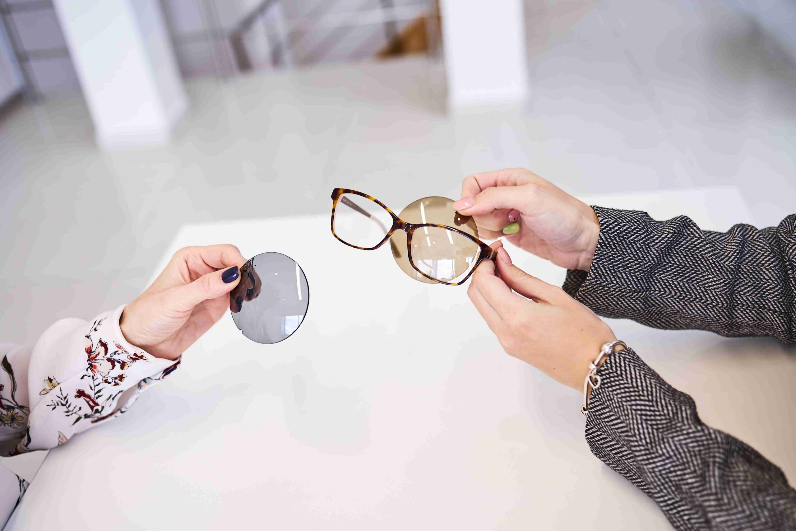 Smiling woman wearing blue glasses, holding and examining a dark pair of frames in Dietz-McLean Optical store in San Antonio.